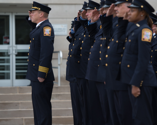 Gruppe von Polizisten in Uniform, die vor einem Gebäude mit Glastüren und Treppe salutieren.