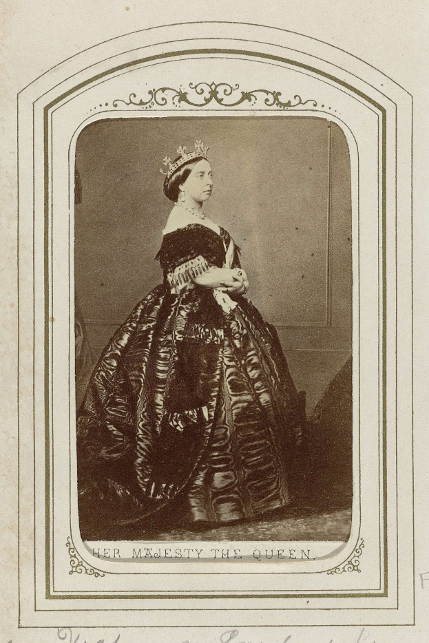 Ein Schwarz-Weiß-Foto einer Frau in einem langen schwarzen Kleid mit einem hohen Kragen, langen Ärmeln und einer juwelenbesetzten Krone, deren Haar elegant hochgesteckt ist.