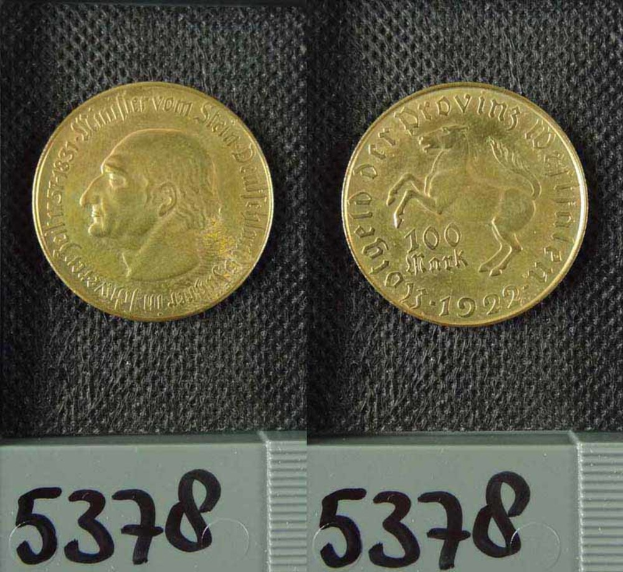 Zwei Goldmünzen aus Deutschland im Jahr 1922, jeweils mit einem Nennwert von 100 Mark, die auf einer schwarzen Oberfläche mit Zahlen unten liegen.