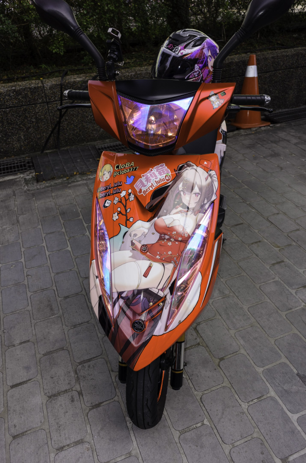 Oranger Roller auf der Straße mit Helm darauf, Verkehrskegel, Wand und Bäume im Hintergrund.