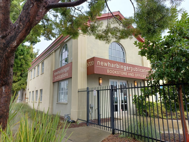Außenansicht der Newharbinger Public Library in San Francisco, Kalifornien, mit einem Gebäude mit Fenstern und Türen, einem Schild, einem Metallzaun, einem Weg, Pflanzen, Bäumen und einem bewölkten Himmel.