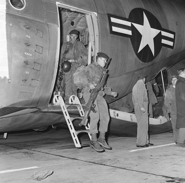 Schwarzes und weißes Foto einer Gruppe von Männern, die auf einem Flugzeug stehen und einer eine Waffe hält.