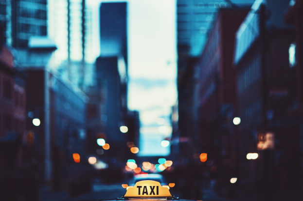 Gelbes Taxi fährt nachts auf einer Stadtstraße, flankiert von Gebäuden mit einem unscharfen Hintergrund.