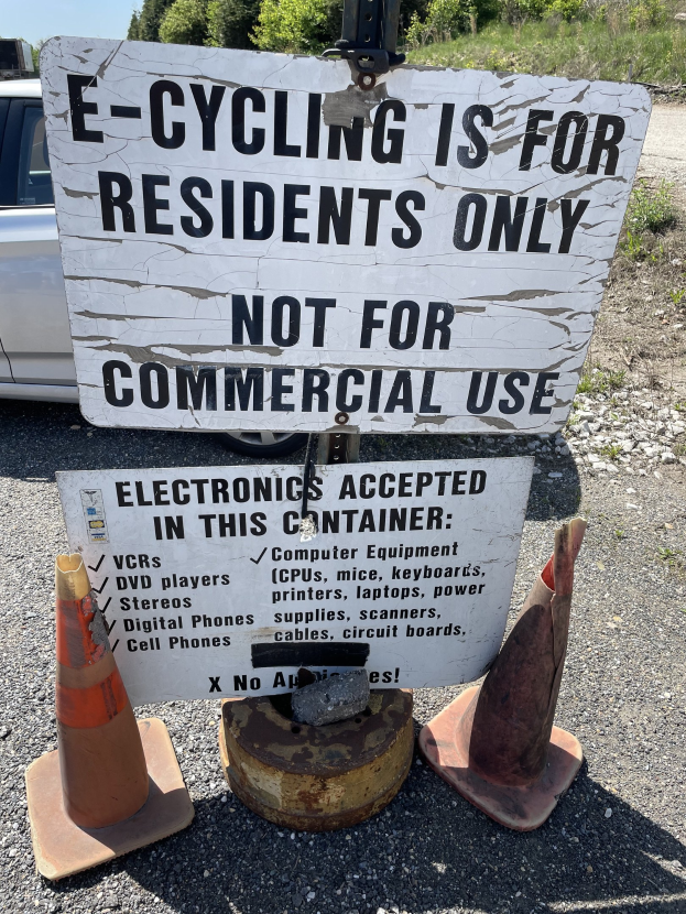 Ein Schild mit der Aufschrift "E-Bike-Fahren ist nur für Anwohner" neben einer Straße mit Verkehrskegeln, einem Fahrzeug, Bäumen und einem klaren blauen Himmel im Hintergrund.