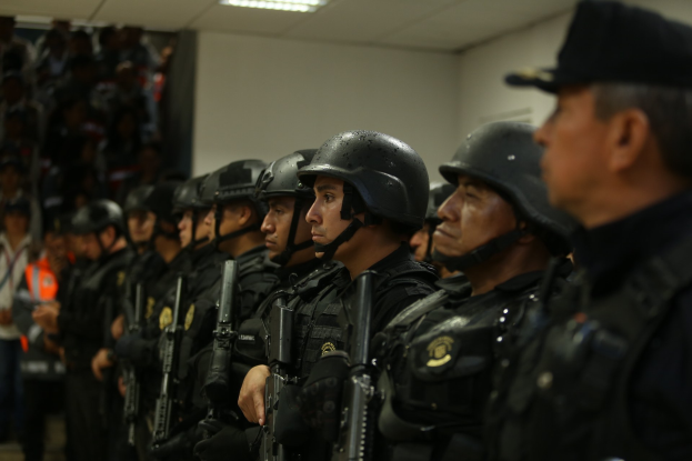 Eine Gruppe von Polizisten in Helmen mit Waffen in der Hand, die neben einer Wand mit Deckenbeleuchtung stehen.