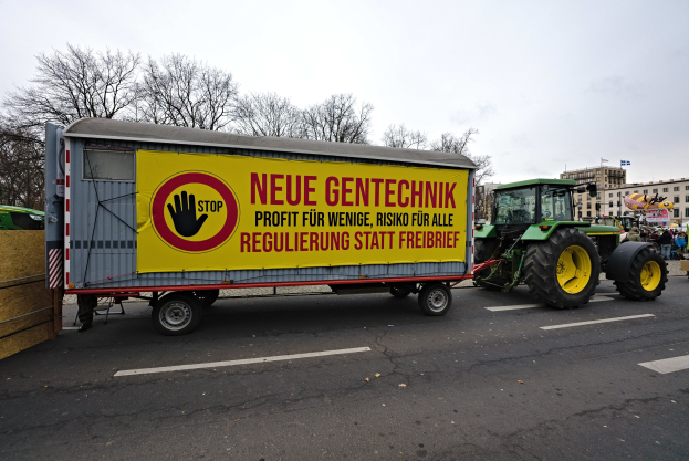 Ein Lastwagen mit einer Tafel fährt eine Straße entlang, umgeben von Menschen, Bäumen, Gebäuden und einem klaren blauen Himmel, wahrscheinlich Teil einer Demonstration in Deutschland.