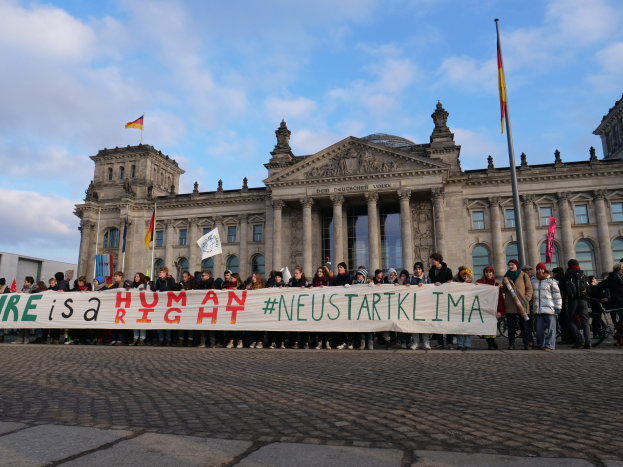 Gruppe von Menschen vor dem Reichstag in Berlin mit einer Fahne, auf der 'Wir sind ein Menschenrecht' steht