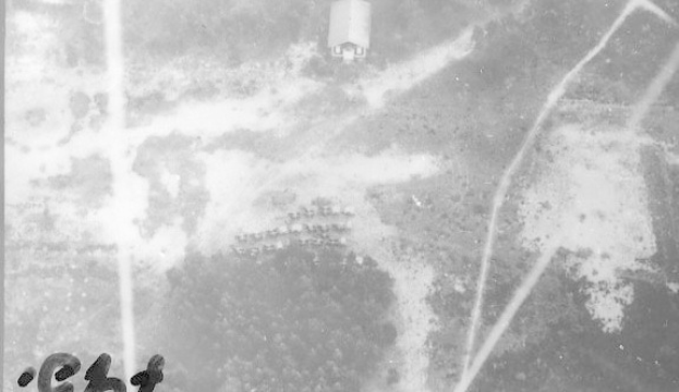 Schwarzes und weißes Foto eines Flugzeugs, das über ein Feld mit einem Gebäude im Hintergrund fliegt und unten den Text 'Zweiter Weltkrieg US-Luftwaffe' trägt.
