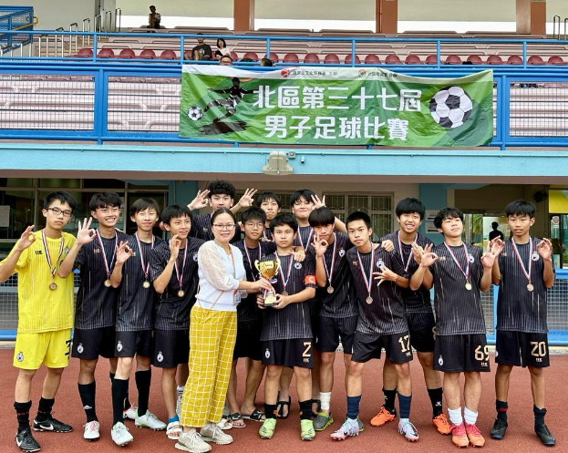 Gruppe junger Männer in Fußballtrikots auf einem Feld, mit Medaillen und einem Pokal, im Hintergrund eine Tribüne und ein Banner 'Yokohama U-16 Boys Soccer Team'.