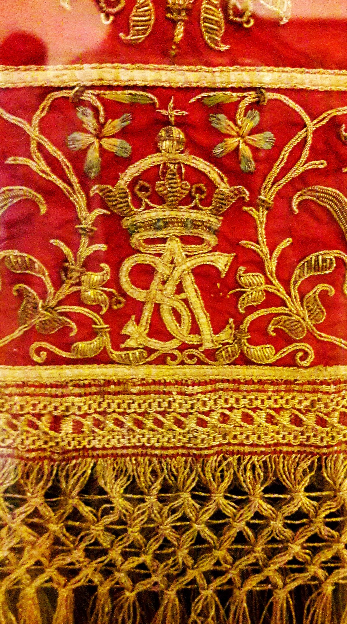 Nahaufnahme eines roten und goldenen Tuchs mit einer Krone und aufwändiger Goldstickerei.