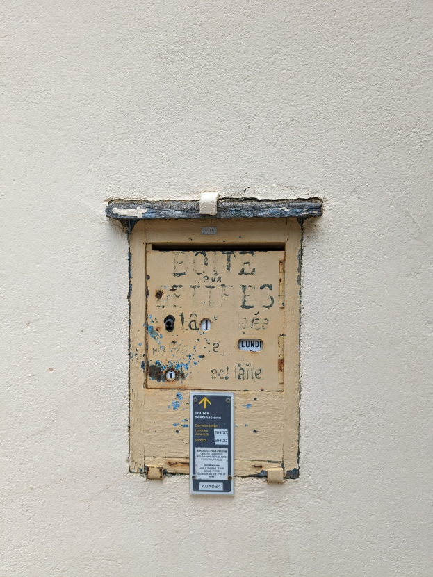 Alte rechteckige Metall-Klingel mit einer oberen Griffleiste, Schlüsselloch und Textschild, an einer verwitterten Wand mit sichtbaren Rissen und Chips montiert.