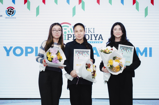 Drei Frauen auf einer Bühne mit Blumensträußen und Urkunden, im Hintergrund ein 'Yopi Diya Awards 2019'-Plakat.