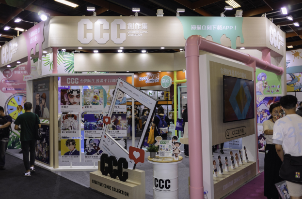 Eine Gruppe von Menschen vor einem Messestand mit Aufbauten, Fernseher und Deckenbeleuchtung, mit Text, der ein kreatives Comic-Sammler-Thema suggeriert.