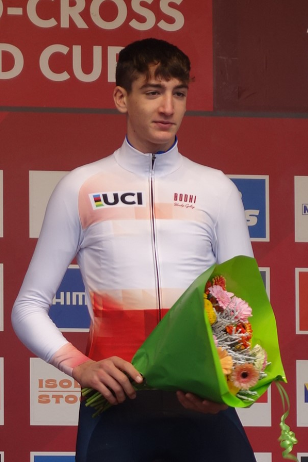 Ein Mann steht triumphierend auf einem Podium, h├Ąlt einen Blumenstrau├č in der Hand und hat eine Tafel im Hintergrund, die Freude und Selbstbewusstsein ausstrahlt.