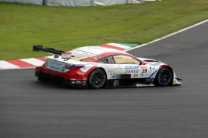 Ein Sportwagen mit Text und Zahlen, der bei den 24 Stunden von Le Mans teilnimmt, fährt auf einer Rennstrecke mit Gras örtlich und einem Zaun im Hintergrund.
