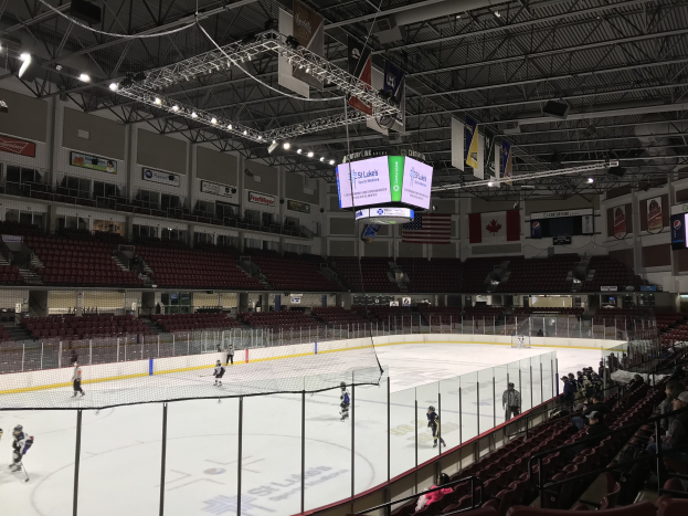 Ein Eishockeyspiel in einer großen Arena mit einem zentralen Netz, Zuschauern auf beiden Seiten, Deckenbeleuchtung und Bannern, identifiziert als die St. Louis Blues Arena.