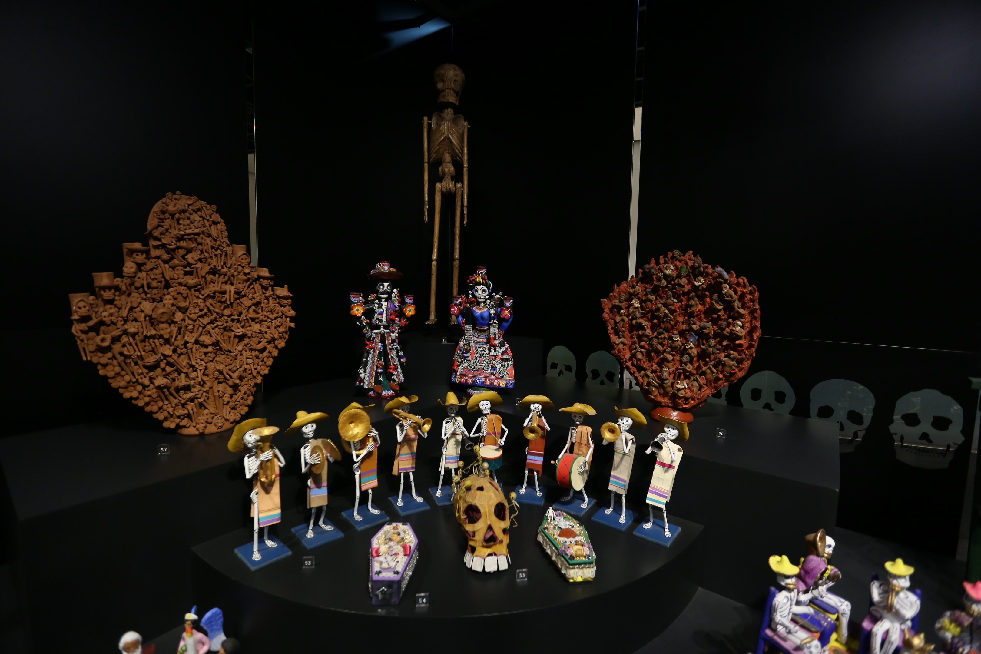 Vitrine mit verschiedenen Spielzeugen, darunter Puppen, Schädel und andere Gegenstände, vor dunklem Hintergrund.