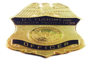 Goldene Abzeichen mit 'U.S. Customs and Border Protection Officer' eingraviert, mittig auf einem weißen Hintergrund.