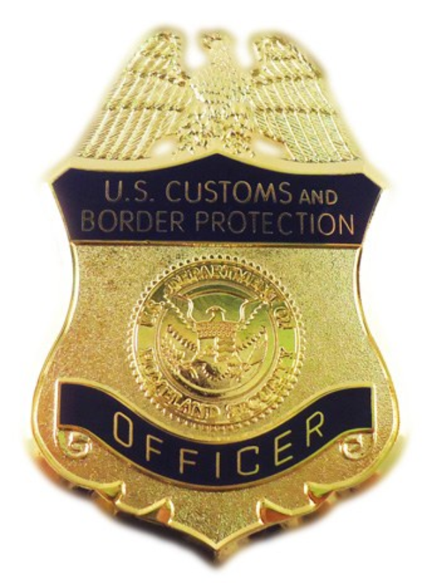 Goldene Abzeichen mit 'U.S. Customs and Border Protection Officer' eingraviert, mittig auf einem weißen Hintergrund.