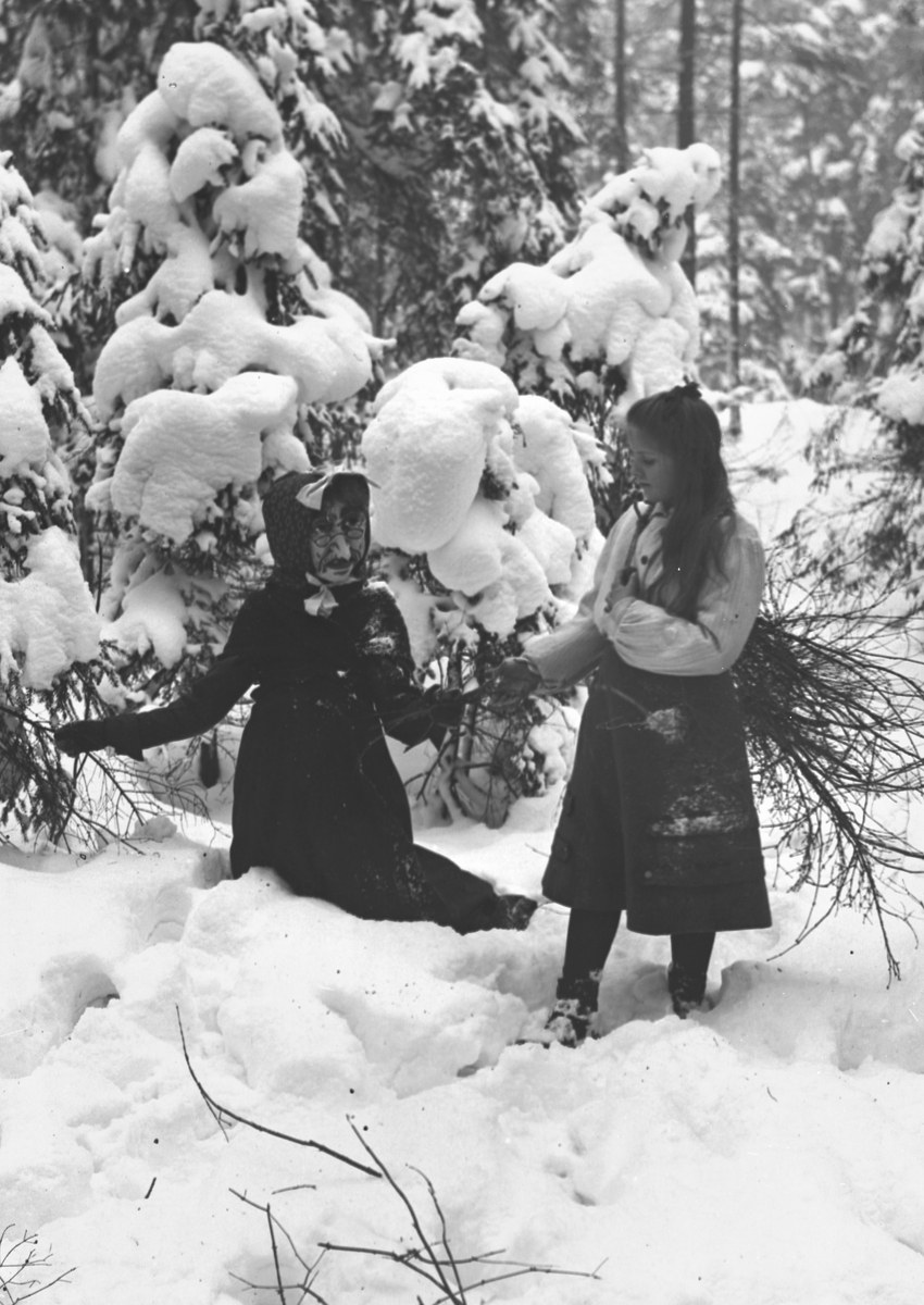 Zwei Kinder beim Spielen in einem verschneiten Waldgebiet, umgeben von schneebedeckten Bäumen, in Schwarz-Weiß.