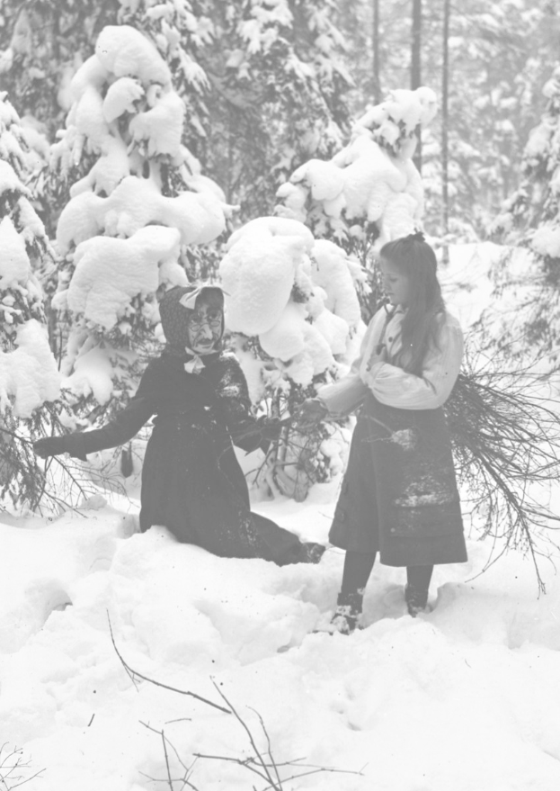Zwei Kinder beim Spielen in einem verschneiten Waldgebiet, umgeben von schneebedeckten Bäumen, in Schwarz-Weiß.