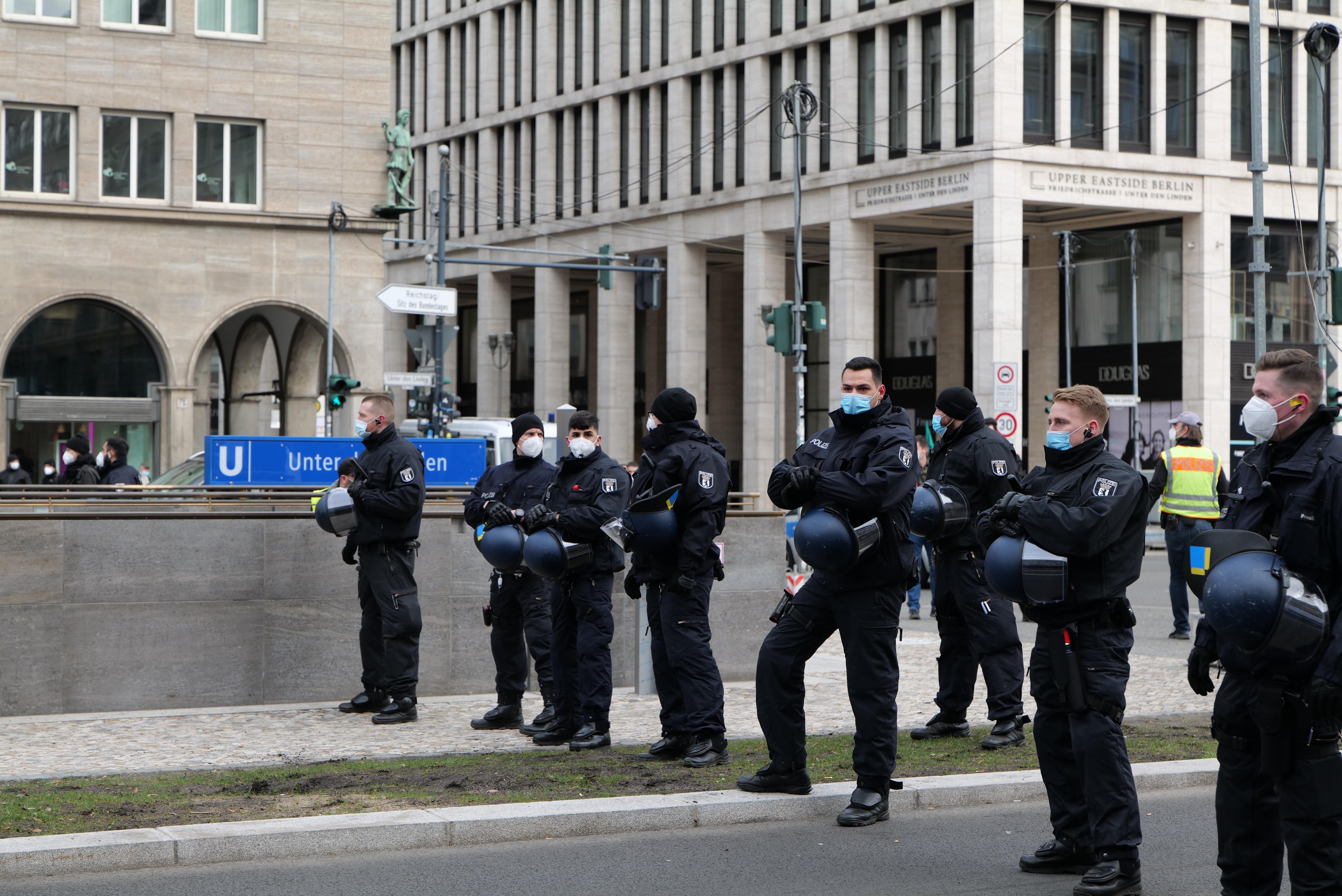 Polizeibeamte in schwarzen Uniformen und Masken stehen vor einem Berliner Gebäude mit Glasfenstern, Säulen und grasbewachsenem Boden.