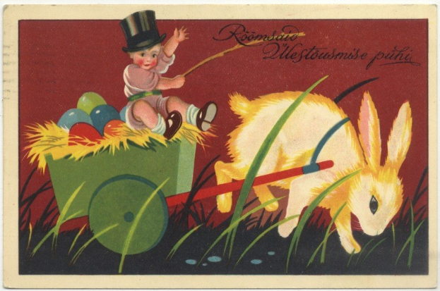 Alte Postkarte mit einem Baby in einem Zylinder, das einen Karren voller bunter Ostereier schiebt, begleitet von einem Hasen, mit handgeschriebener Ostergrüß.