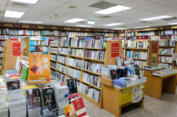 Ein gut organisierter Buchladen mit Regalen und Tischen voller Bücher, Informationsschildern auf dem Boden und Deckenleuchten.