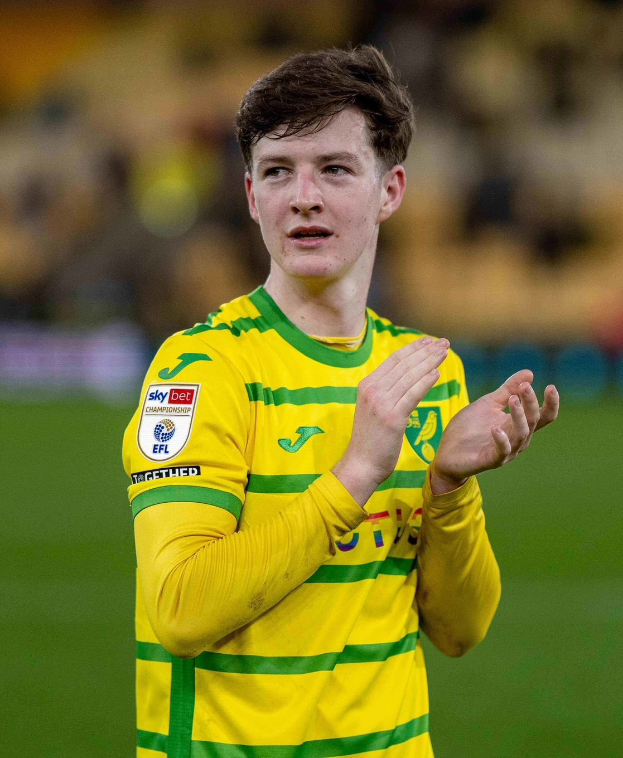 Ein junger Mann in einem gelb-grünen T-Shirt feiert auf einem Fußballfeld, indem er jubelnd die Hände zusammenklatscht, während ein unscharfer Hintergrund seine freudige Reaktion auf das erzielte Tor betont.