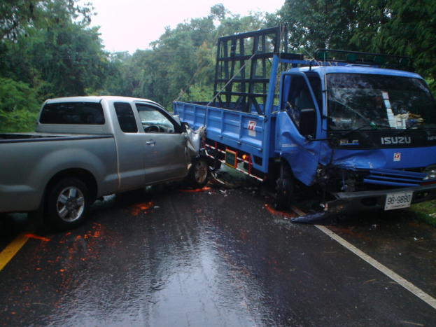 Ein schwerbeschädigter Lkw mit eingedrückter Front und verbeulter Karosserie am Straßenrand, umgeben von Bäumen unter einem klaren blauen Himmel.