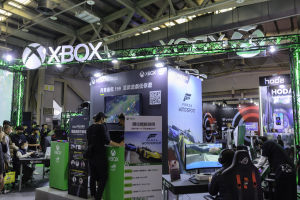 Eine Gruppe von Menschen an einem Messestand für "Forza Motorsport 5 China", mit Tischen, die Monitore und Tastaturen anzeigen, umgeben von Bannern und einem Metallgestell im Hintergrund.