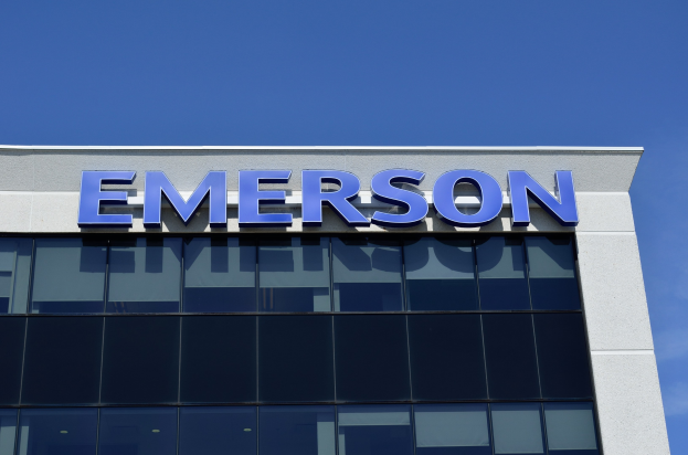 Emerson-Logo an einer Gebäudeaussenseite mit Text, der "Emerson investiert 1,5 Milliarden USD in den USA" angibt, vor einem klaren blauen Himmel.