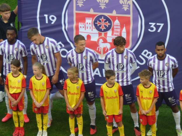 Eine Gruppe junger Menschen auf einem Fußballfeld mit einem Banner im Hintergrund, auf dem "Preston Primary School Football Team" steht.