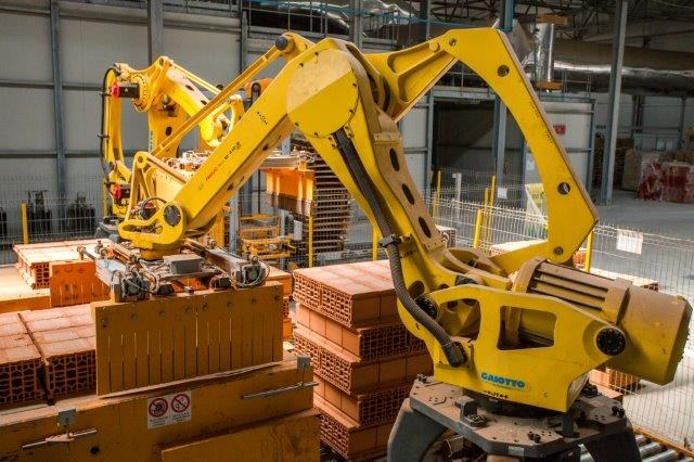 Großes Industriegebäude mit gestapelten Kisten, Kränen, Zaun, Pfählen und einer fernen Wand in einer automatisierten Fertigungsumgebung.