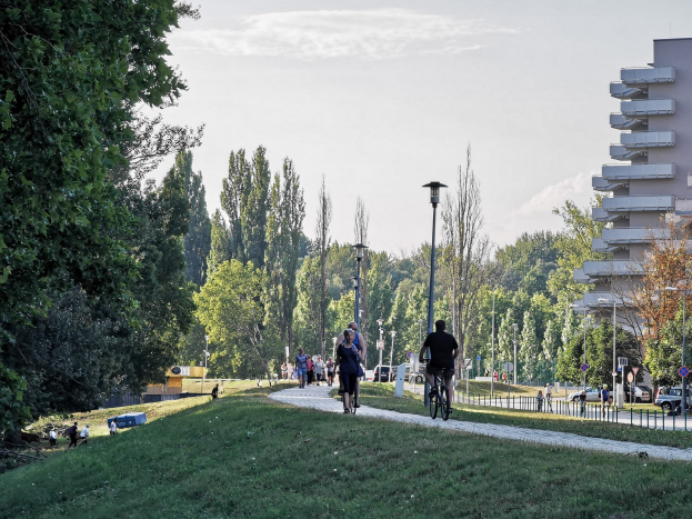 Gruppe von Menschen, die Fahrräder auf einem Parkweg mit Bäumen, Straßenlaternen und Gebäuden im Hintergrund fahren