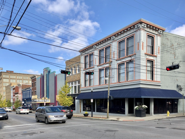 Eine Stadtstra├čen-Szene mit parkenden Autos, Strommasten, Ampeln, Laternen, B├Ąumen und Geb├Ąuden unter einem bew├Âlktem Himmel, mit Text, der ein kommerzielles Grundst├╝ck zum Verkauf f├╝r $1,250,000 anzeigt.