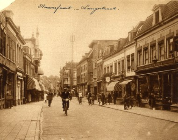 Altes Schwarz-Weiß-Foto von Menschen, die Fahrräder auf einer Straße mit Gebäuden auf beiden Seiten fahren, und Text oben.