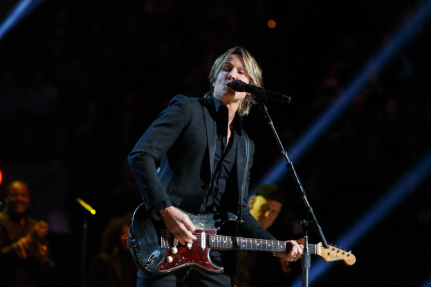 Keith Urban auf der Bühne im Joint in Las Vegas, spielt eine Gitarre mit einem Mikrofon davor und Musikern im Hintergrund, unter dunkler Beleuchtung.