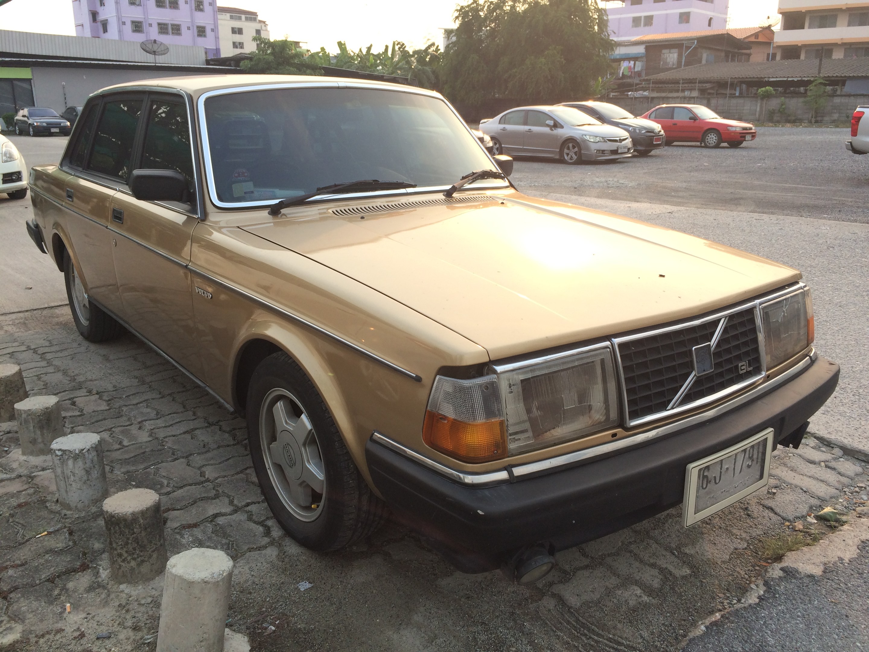 Ein goldfarbener Wagen am Straßenrand mit Gebäuden, Bäumen und einem klaren blauen Himmel im Hintergrund.