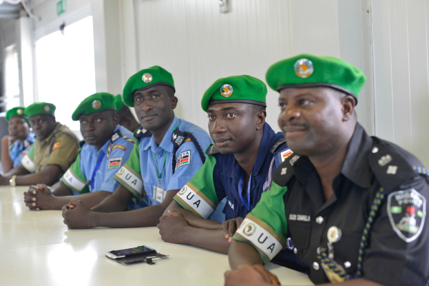 Gruppe von Polizeibeamten an einem Tisch während einer Schulung, mit Mobiltelefonen und anderen Gegenständen auf dem Tisch, in einem Raum mit Fenstern und Deckenleuchten.