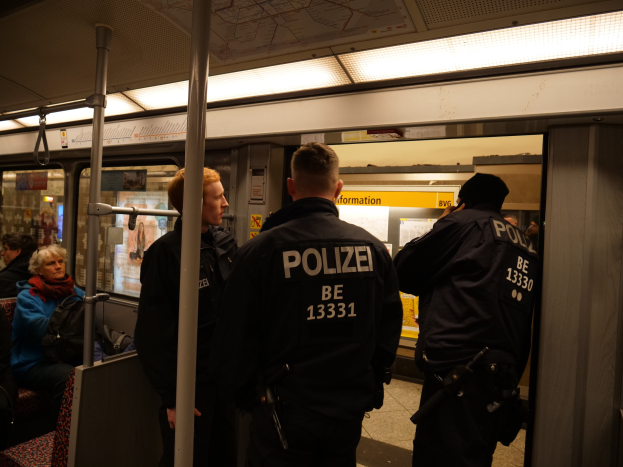 Eine Gruppe von Polizisten steht neben sitzenden und stehenden Passagieren in einem hell erleuchteten U-Bahn-Zug.