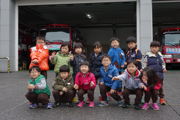 Kinder vor einer Feuerwache mit Feuerwehrautos in der Garage und einem Geländer auf der linken Seite.
