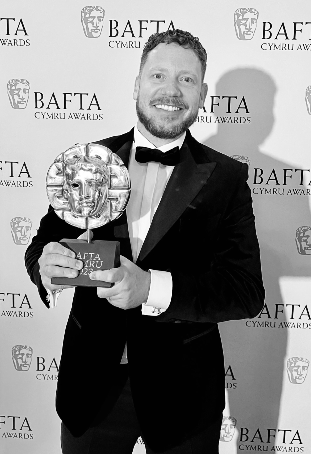 Ein Mann im Smoking, der eine BAFTA-Auszeichnung hält und lächelt, vor einer Hintergrundtafel mit der Aufschrift "BAFTA Awards 2018."