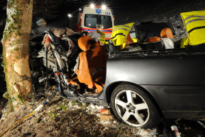 Ein beschädigtes Auto am Straßenrand auf einer schneebedeckten Straße mit einem im Hintergrund sichtbaren Rettungswagen.