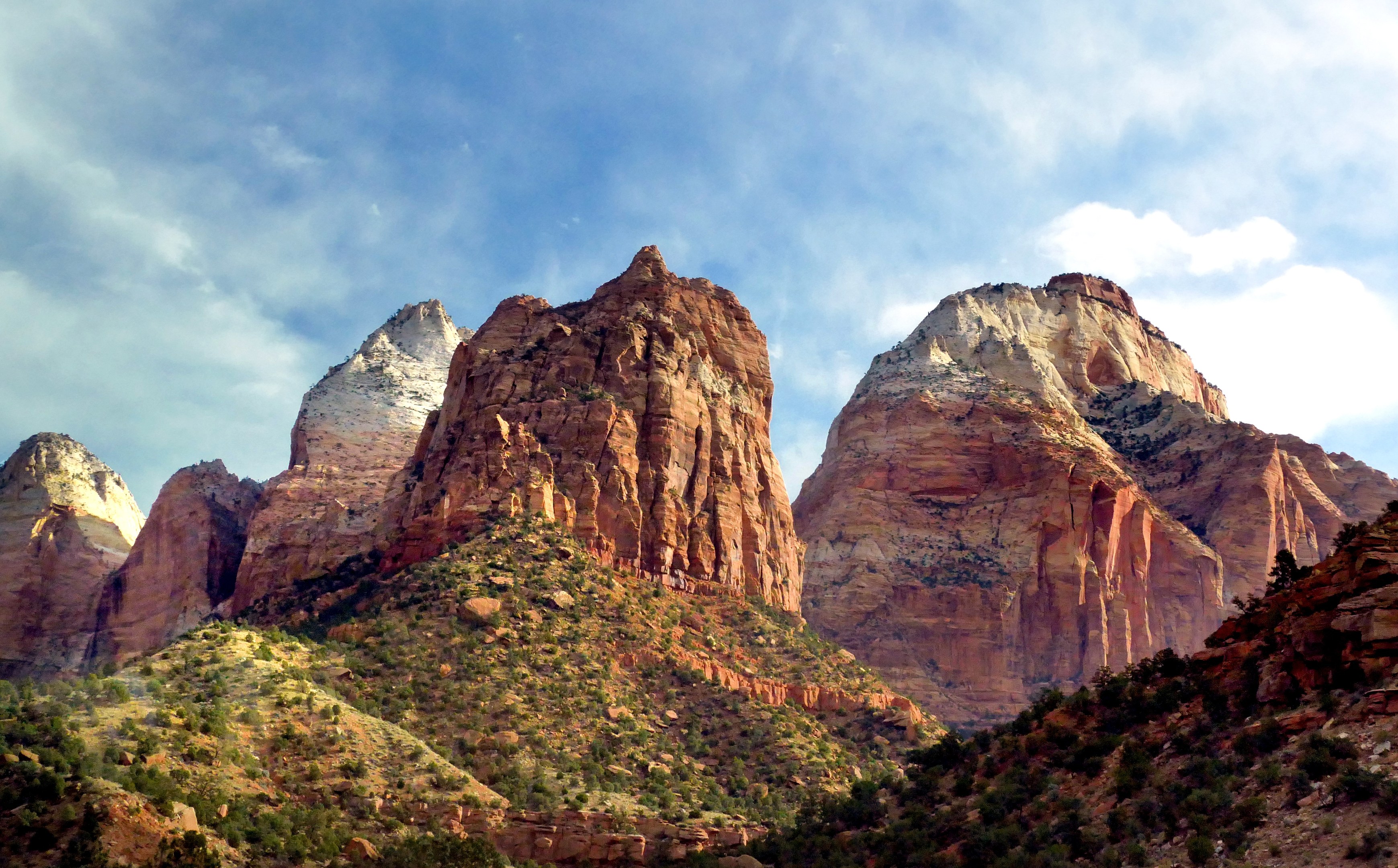 Ein malerischer Blick auf den Zion-Nationalpark in Utah mit majestätischen Bergen, üppigen Bäumen, steiniger Landschaft und einem Himmel mit weißen, flauschigen Wolken.