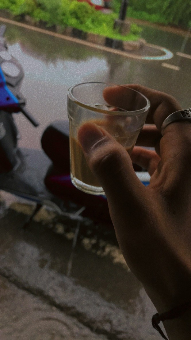 Eine Person mit einem Bierglas vor einem Fenster, daneben ein Motorroller und im Hintergrund Bäume, Masten und eine Straße.