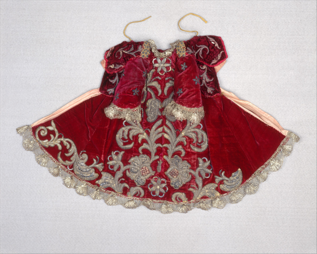 Ein rotes Samtkleid mit goldener Stickerei und detaillierten Designs auf einem Bügel gegen einen weißen Hintergrund.