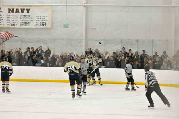 Eishockey-Spieler in Helmen und Uniformen konkurrieren auf einem Eisstadion mit Zuschauern auf den Tribünen und einer Bannerwand im Hintergrund.