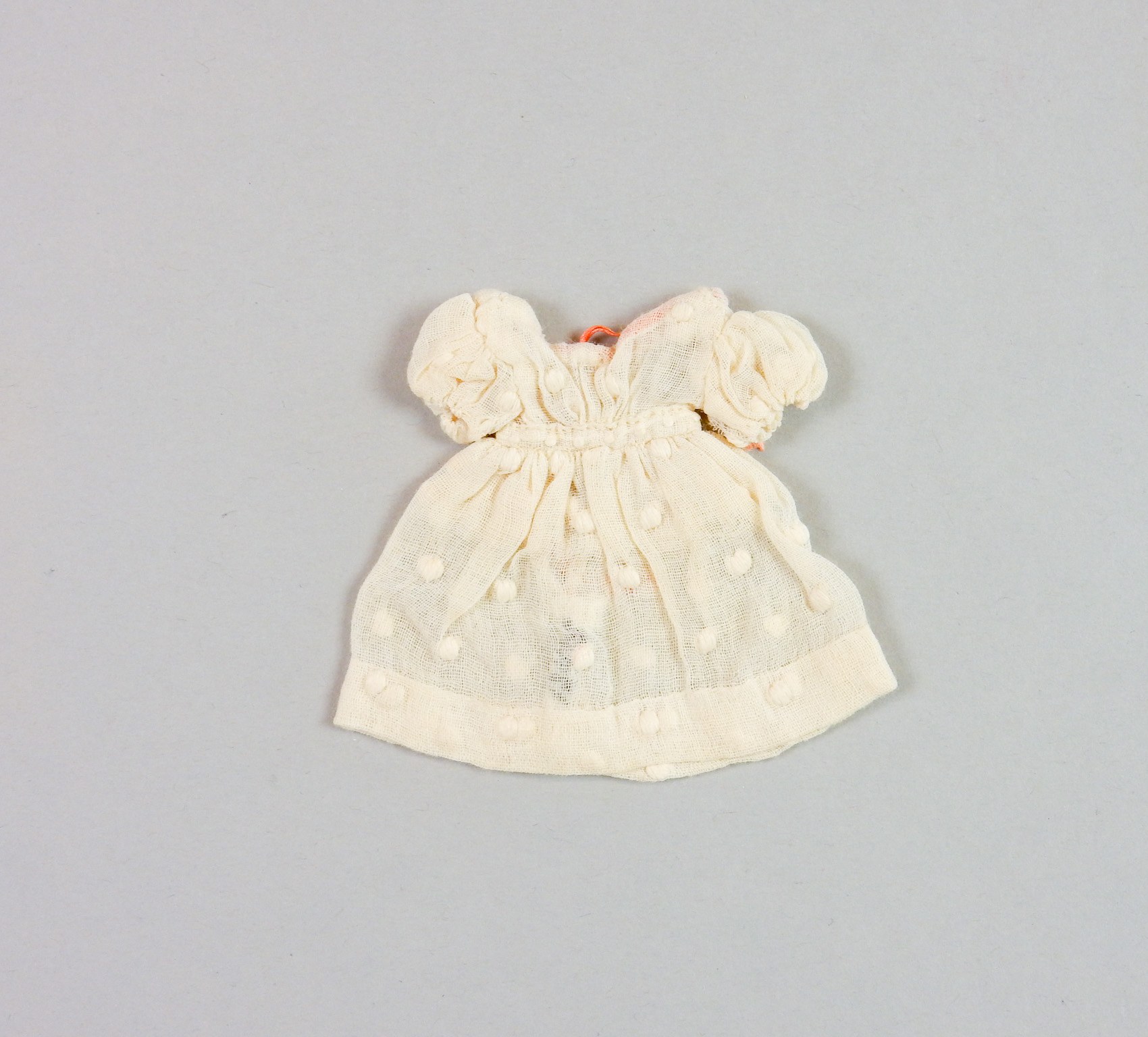 Ein kleines weißes Kleid mit rundem Halsausschnitt, kurzen Ärmeln und einem knielangen Saum, das ein zartes Muster auf leichtem, luftigem Stoff aufweist, der leicht gekräuselt erscheint.