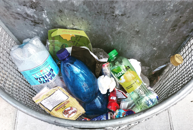 Ein Metallmüllcontainer voller Plastikflaschen, Tüten und diverser anderer Gegenstände.